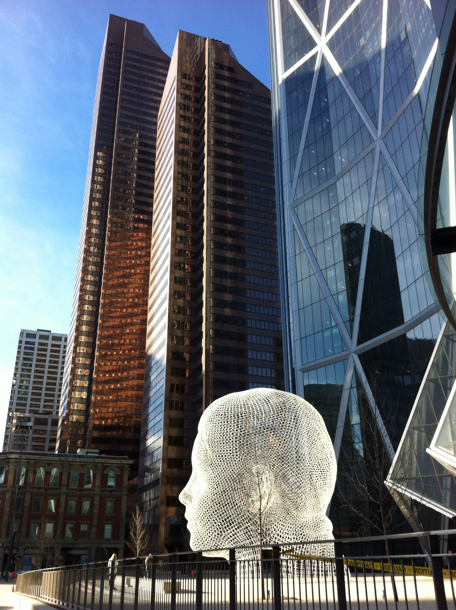 This photo captures the new Wonderland sculpture by Jaume Plensa on the plaza of the Norman Foster Bow Tower. In the background is the Suncor Centre (built in the '80s), which consists of two towers the tallest one was the tallest in Calgary until the Bow was constructed. The Suncor Tower has an interesting slanted roof top and the two towers together make a reference in their design to the iconic prairie grain elevator.