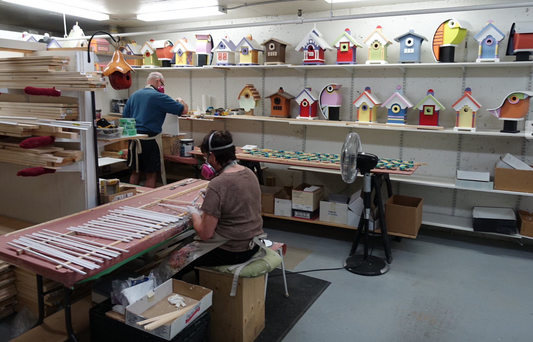 Volunteers from the building help JR with the painting and assembling. Note other birdhouse designs on the shelves in the background.