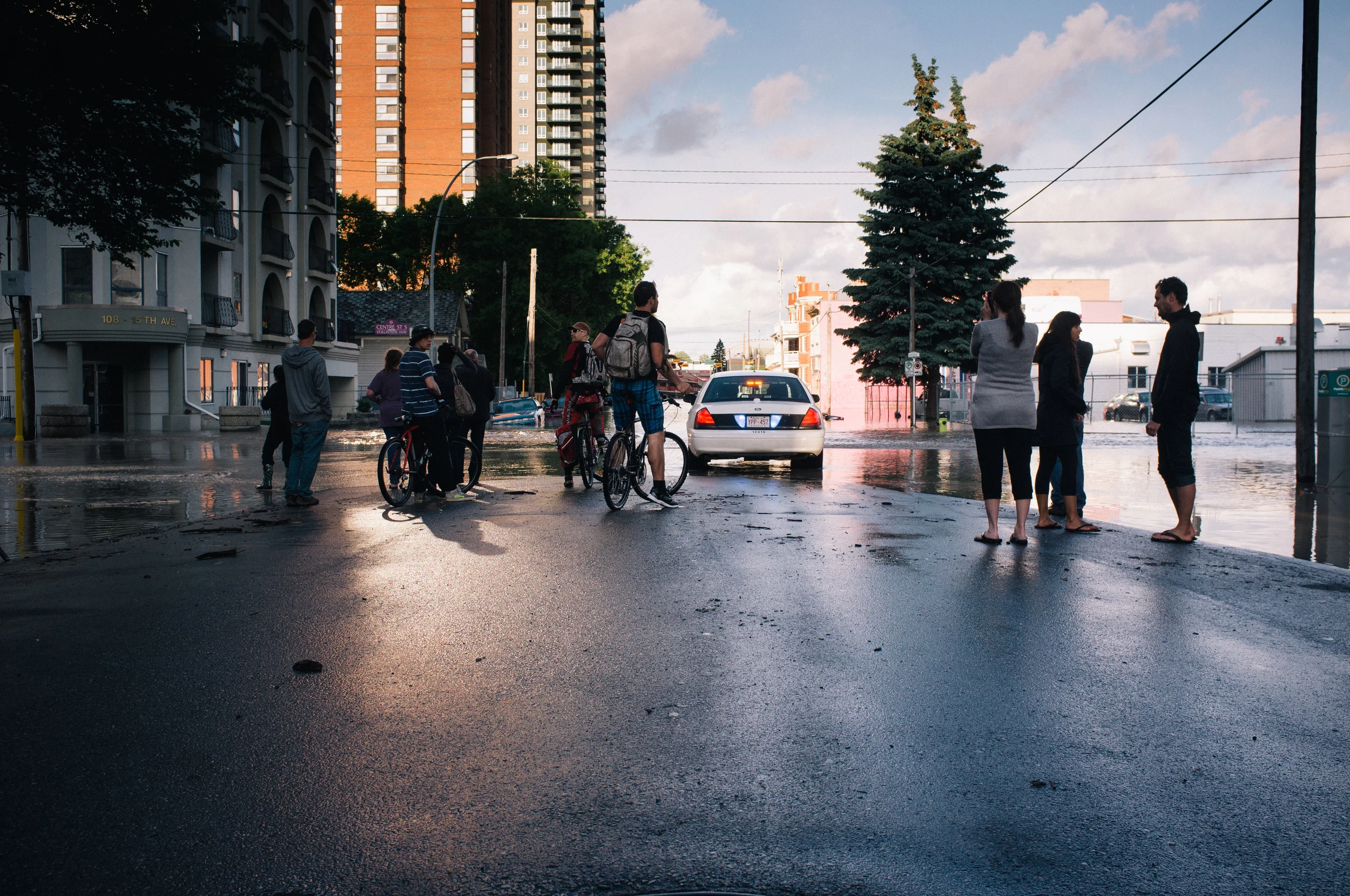 Sightseers. Centre Street at 15 Ave SW, facing the Stampede Grounds. Around the corner, a car was swamped; much debris had accumulated around it in the heavy, northbound current.
