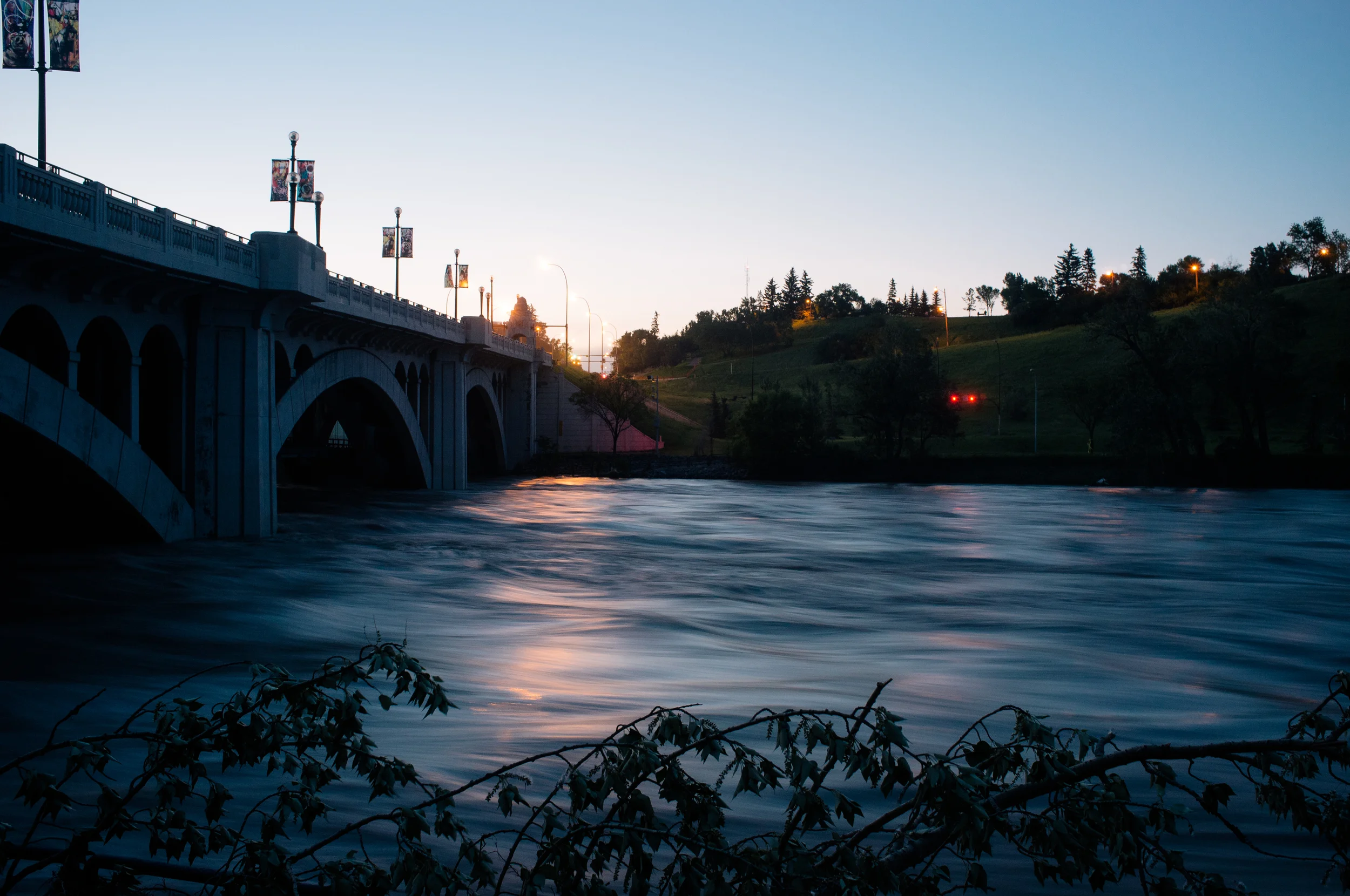 Sunset over the Centre Street Bridge. A downed tree, swept in by the current, lies in the foreground.