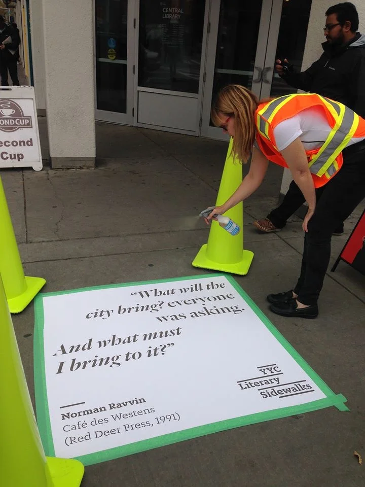 WordFest's Shelley Youngblut spraying a passage from Norman Ravvin's 1991 Calgary novel, Café des Westens , in front of the Central Library.