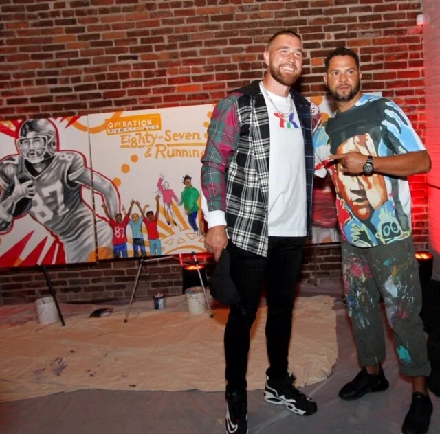 Travis Kelce and Kyle Holbrook in front of the live mural keystone auction item at “Walk the Walk Fashion Show”
