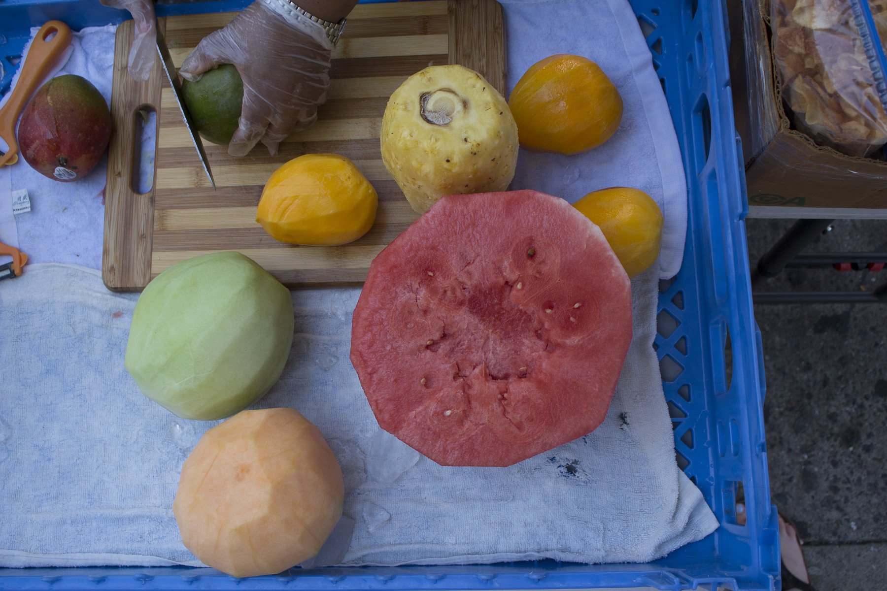  Teodosia is peeling mangoes, honeydew, cantaloupe, pineapple, and watermelon in preparation to cut and pack to sell. She buys her fruit from various places. August 22nd, 2017 Sunset Park, Brooklyn. 