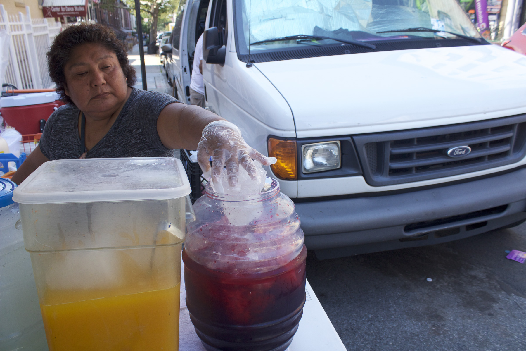 Teodosia putting the chunks of ice she cut into the jamaica on a hot day in Sunset Park, Brooklyn. August 22nd, 2017.