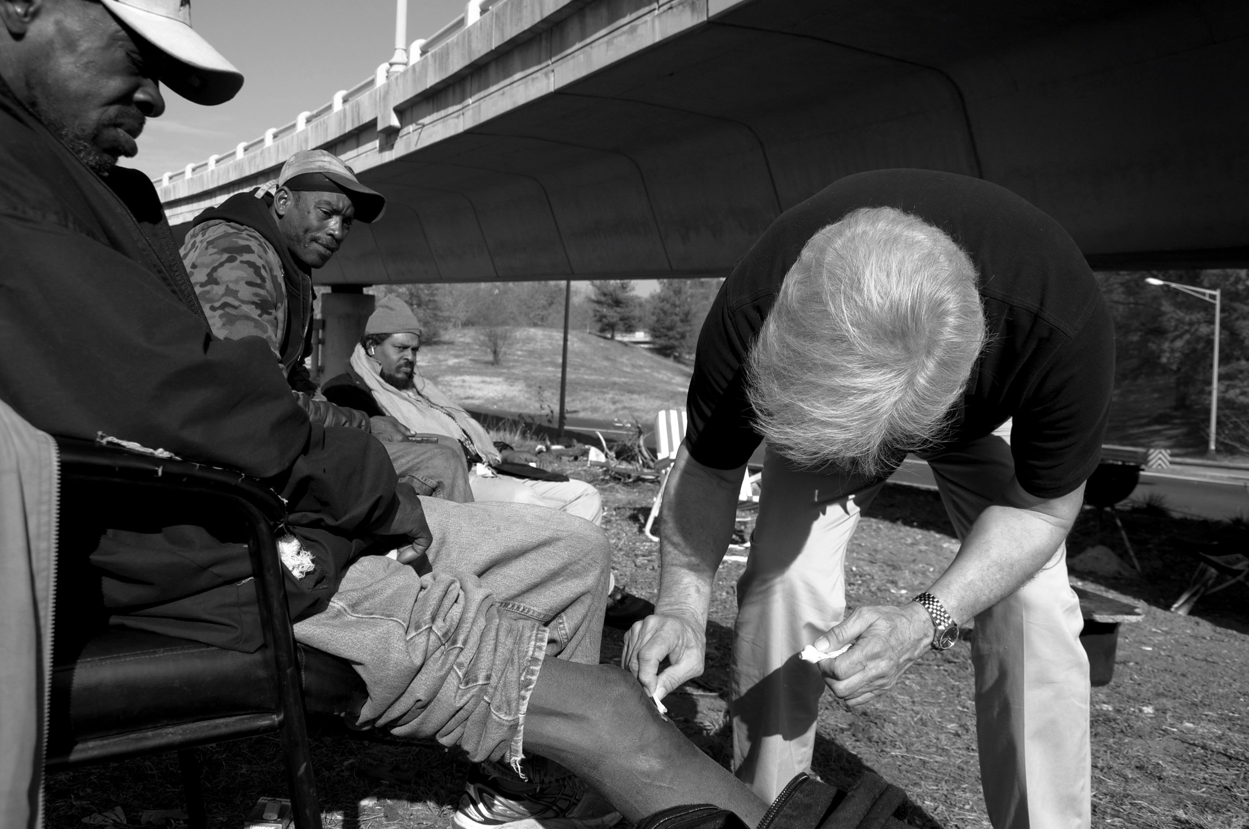  Sitting below an overpass, Willie Brown and his two friends listen to the radio and watch Dr. Anthony Martinez apply Neosporin to Brown's cut knee. Brown injured himself after he fell down an open sewer and plans to sue PEPCO. 