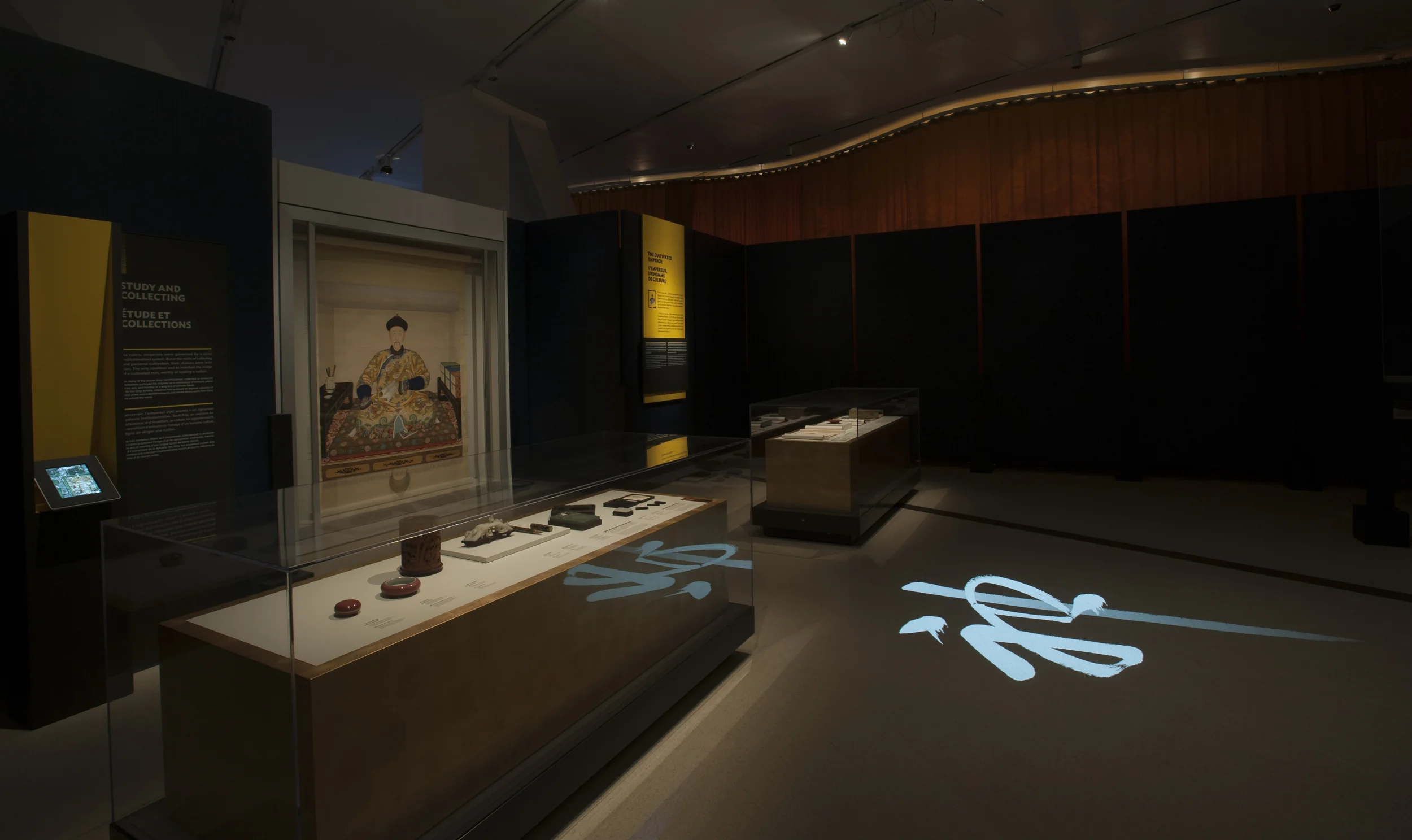  Chinese calligraphy characters animate, as if painted by brushstrokes, onto floor of exhibit space filled with the art of Chinese emperors. The characters themselves represent the reviews bestowed by a historical emperor upon the art of his court (a