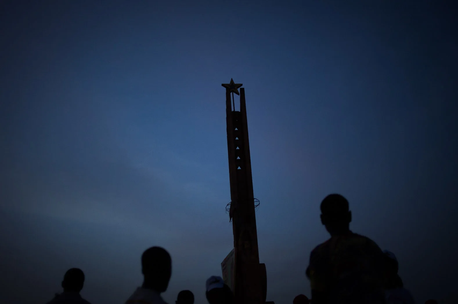 People stand around a monument in Praça dos Heróis Nacionais (National Heroes Square) - a communist monument transformed on independence - at dusk. Guinea Bissau's future is uncertain. Following the April 2012 coup, the military rule the country, and some of the top ranking military are wanted for drug trafficking.
