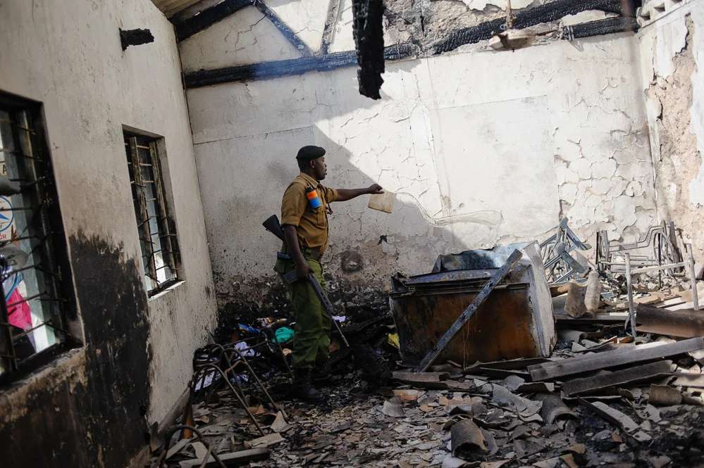 A Kenyan security officer pours water on the smouldering remnants of a church office, burned in riots following the killing of Sheikh Ibrahim