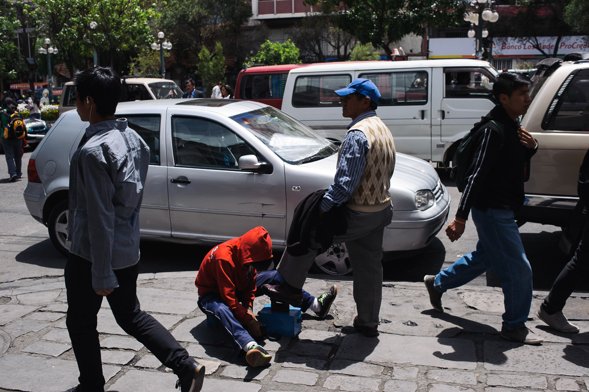 Ruben Flores (13) shines the shoe of a man in the street of central La Paz, Bolivia, as pedestrians walk past.