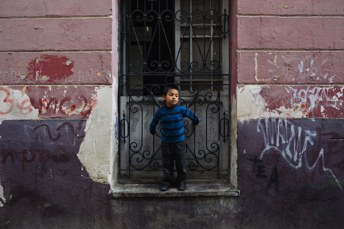 Jonny, Ruben's five year old brother, stands in a window of the "New Day Foundation" as his brother plays football in the street in La Paz, Bolivia.