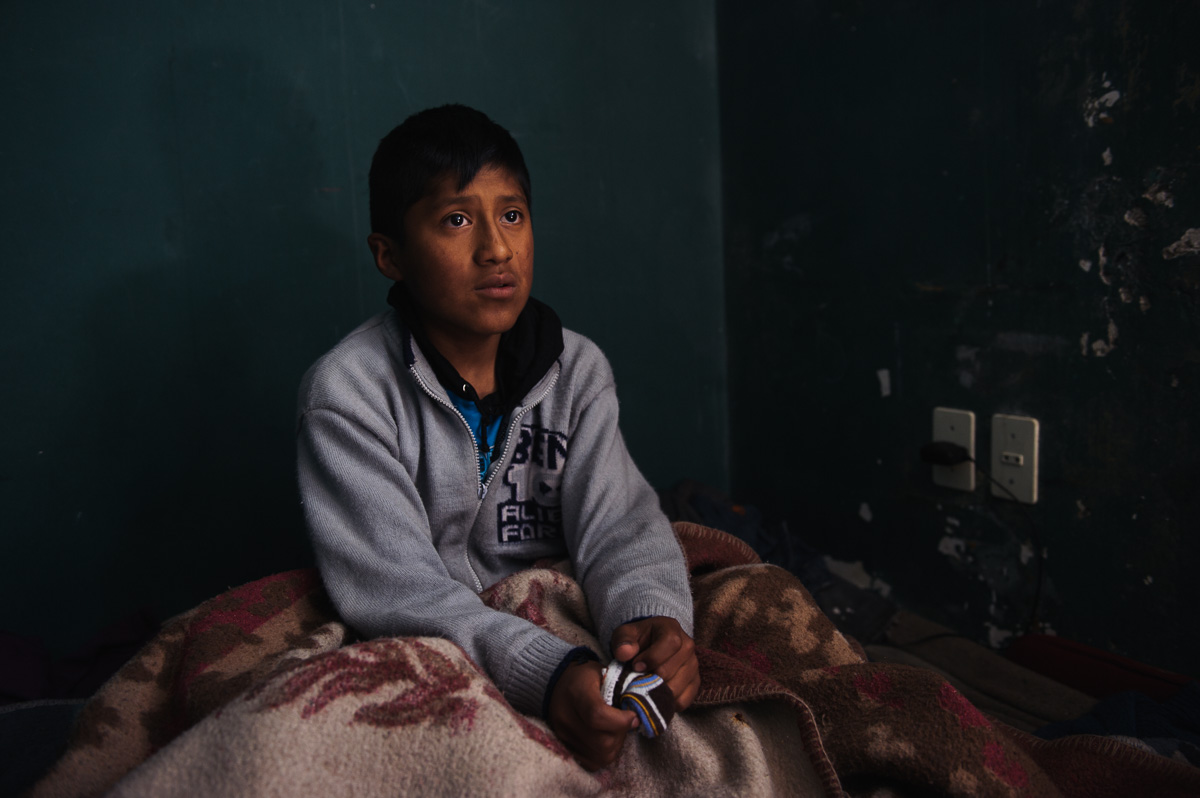 Ruben Flores (13), a shoe-shiner in La Paz, sits in the bed he shares with his four siblings and parents at the "New Day Foundation" association in La Paz, Bolivia, on December 5, 2014. Ruben works as a shoe-shiner in the Bolivian capital, helping to support his family with his earnings.
