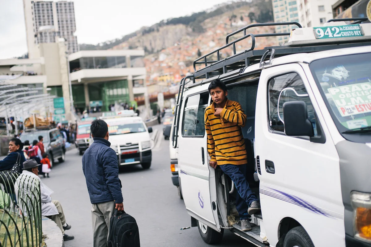 A young boy works as a "vocedore", touting for minibus passengers at a bus-stop in La Paz, Bolivia. As well as calling the bus route to passengers and potential clients, the vocedores open and close the minibus door, a job deemed "hard labour" and forbidden for young children.