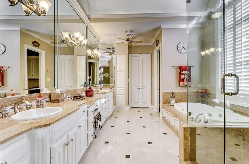 A spacious bathroom with double sinks, large mirror, and a whirlpool bathtub next to a window with blinds.