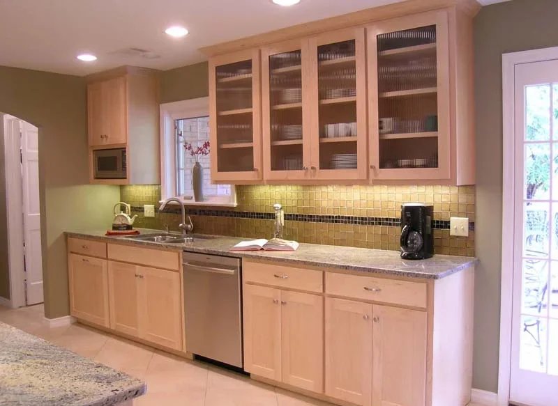 Kitchen with light wooden cabinets, a granite countertop, a window with a vase, a coffee maker, and a cookbook on the counter.