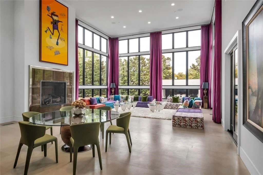 Modern living room with large windows, purple curtains, colorful pillows, and a glass dining table with green chairs.
