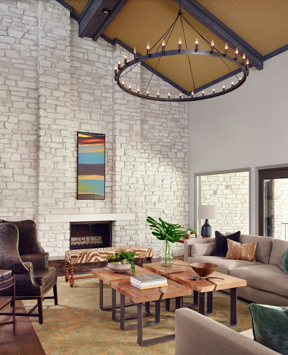 Living room with white brick fireplace, modern furniture, a large circular chandelier, and abstract art on the wall.
