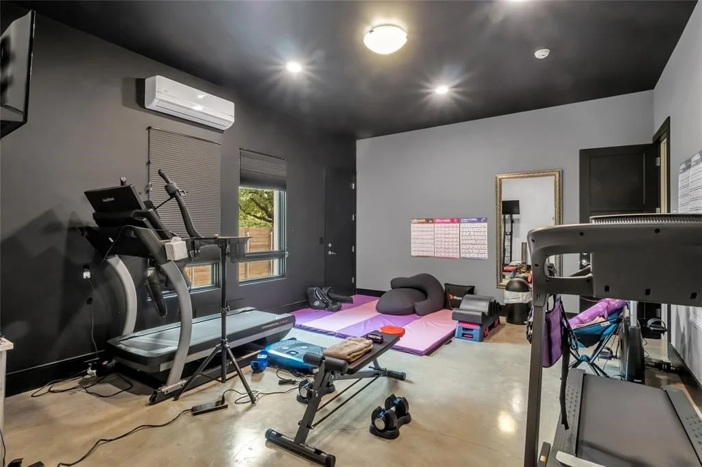 Home gym with treadmill, punching bag, yoga mats, and workout equipment, with windows, mirror, and wall calendar.