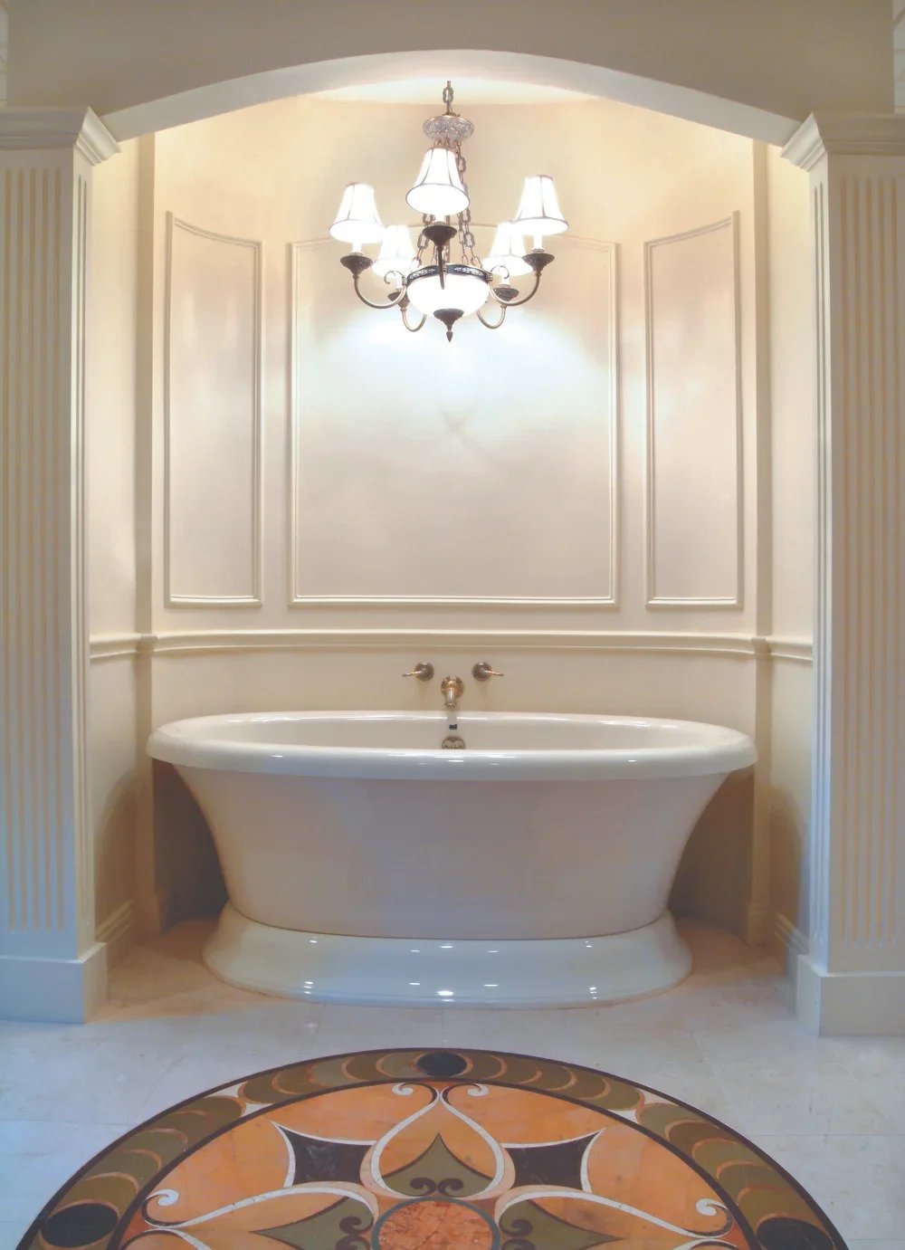 Elegant bathroom with a freestanding bathtub, chandelier, and decorative wall panels, viewed from a circular tile floor.