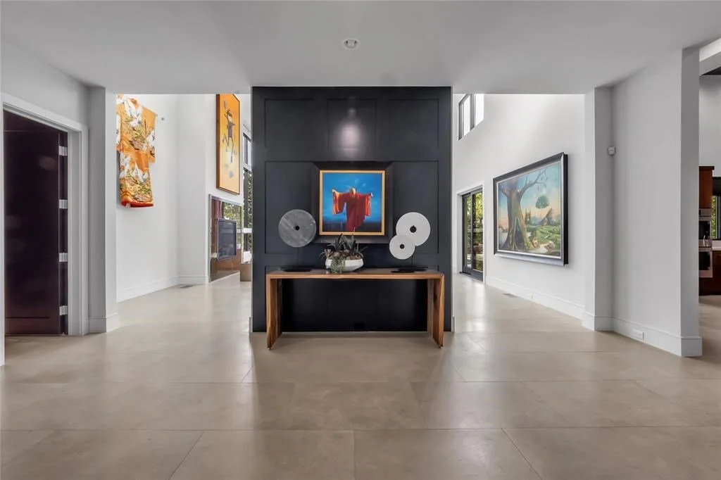 Modern art gallery interior with white walls, hardwood and tile floors, and artworks including paintings and sculptures displayed on walls and surfaces.