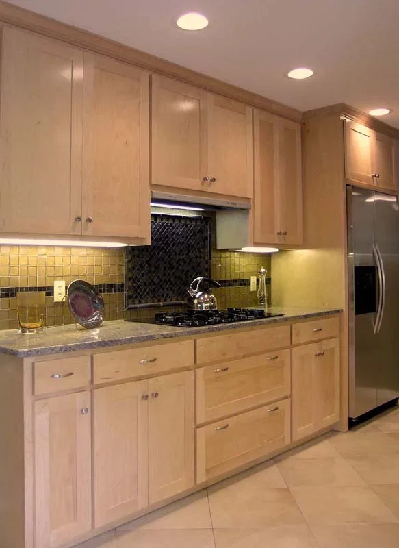 Modern kitchen with light wood cabinets, granite countertop, black tile backsplash, stainless steel refrigerator, and a gas stove with a kettle on it.