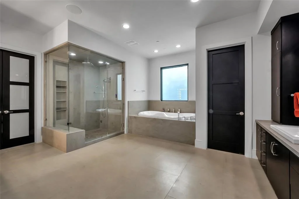 Modern bathroom with glass shower, bathtub, and dark cabinets.