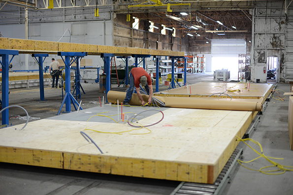 The floor is taken off of the jacks and placed onto rollers, the floor from this point on will be slid along these rollers and pieces will be craned onto the platform. The linoleum flooring is now placed first. Since we’re in a factory environment there is no concern about installing the floor prior to the townhome being dried in. Putting the floor down before the framing make it easier to install, minimizing cuts around walls and cabinetry. Carpet will be installed near the very end since it’s more difficult to protect during construction.