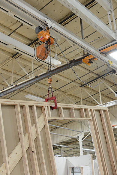 The initial framed walls are craned into place with overhead rolling cranes. While the remaining walls are framed in station 4; electrical work begins, bringing in wiring and junction boxes for fire control systems, and outlets. Plumbing is routed vertically and other connections are made for sanitary wastewater lines. Fire control boxes are installed an conduit pull runs are installed for routing of all conduit to be installed in the field.