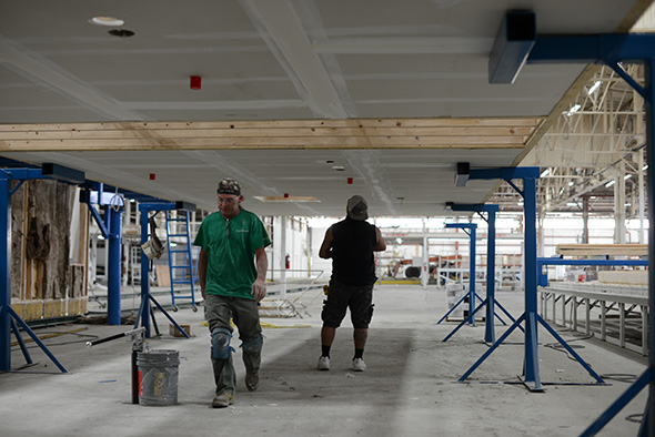 Just before the floor platform in station 4 is moved into its next position at station 8. Electrical Junction Boxes and stubouts for fire suppression sprinkler heads are installed. The drywall for the ceiling is also taped and mudded prior to the entire assembly being craned over the box in Station 8.