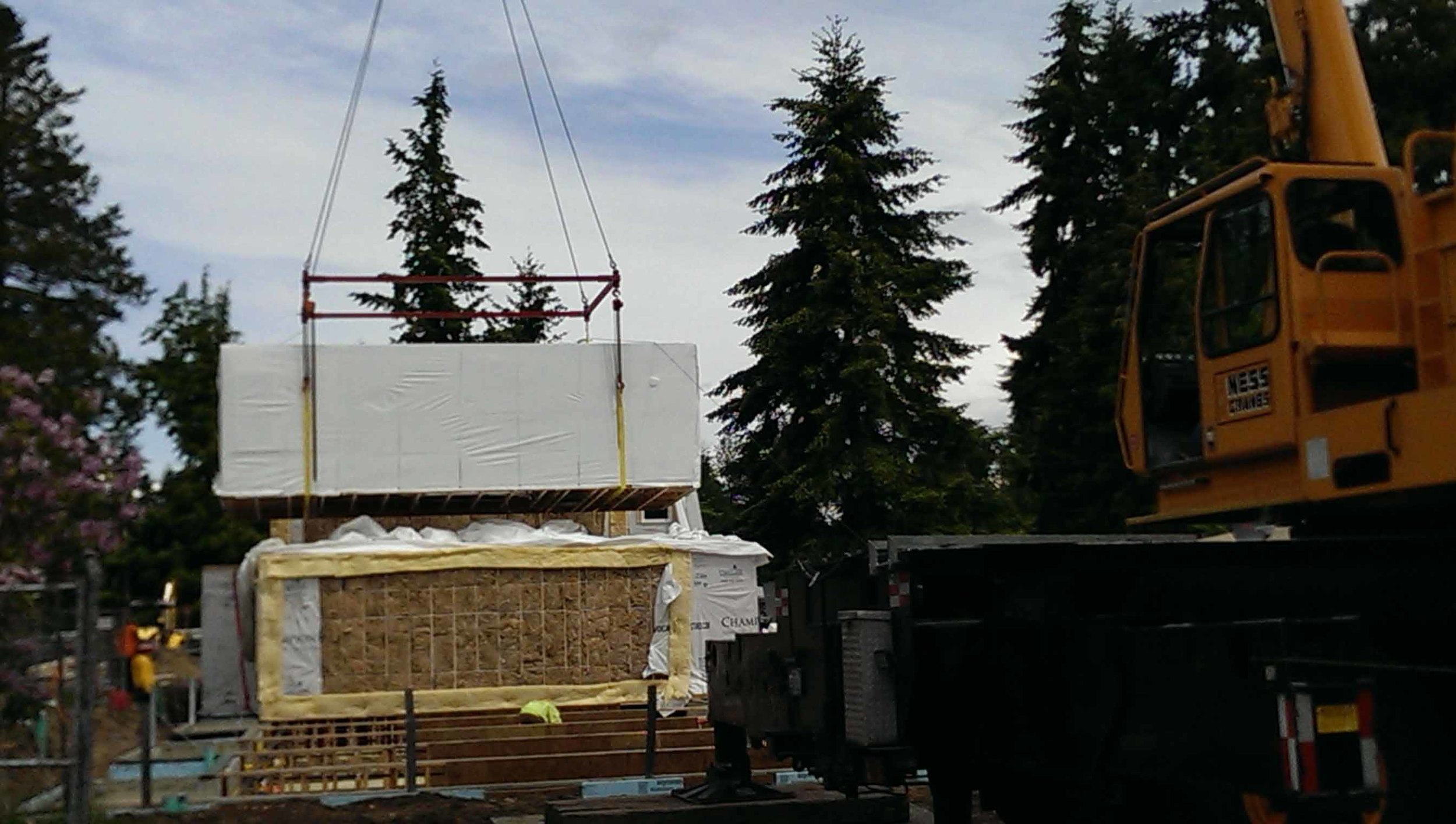 As the boxes come along a separate crew follows up and places batt insulation, shown here in yellow, the insulation acts as a fire/smoke separation between units. Additionally, crews mechanically attach straps which structurally tie the modules to the foundation and to each other.
