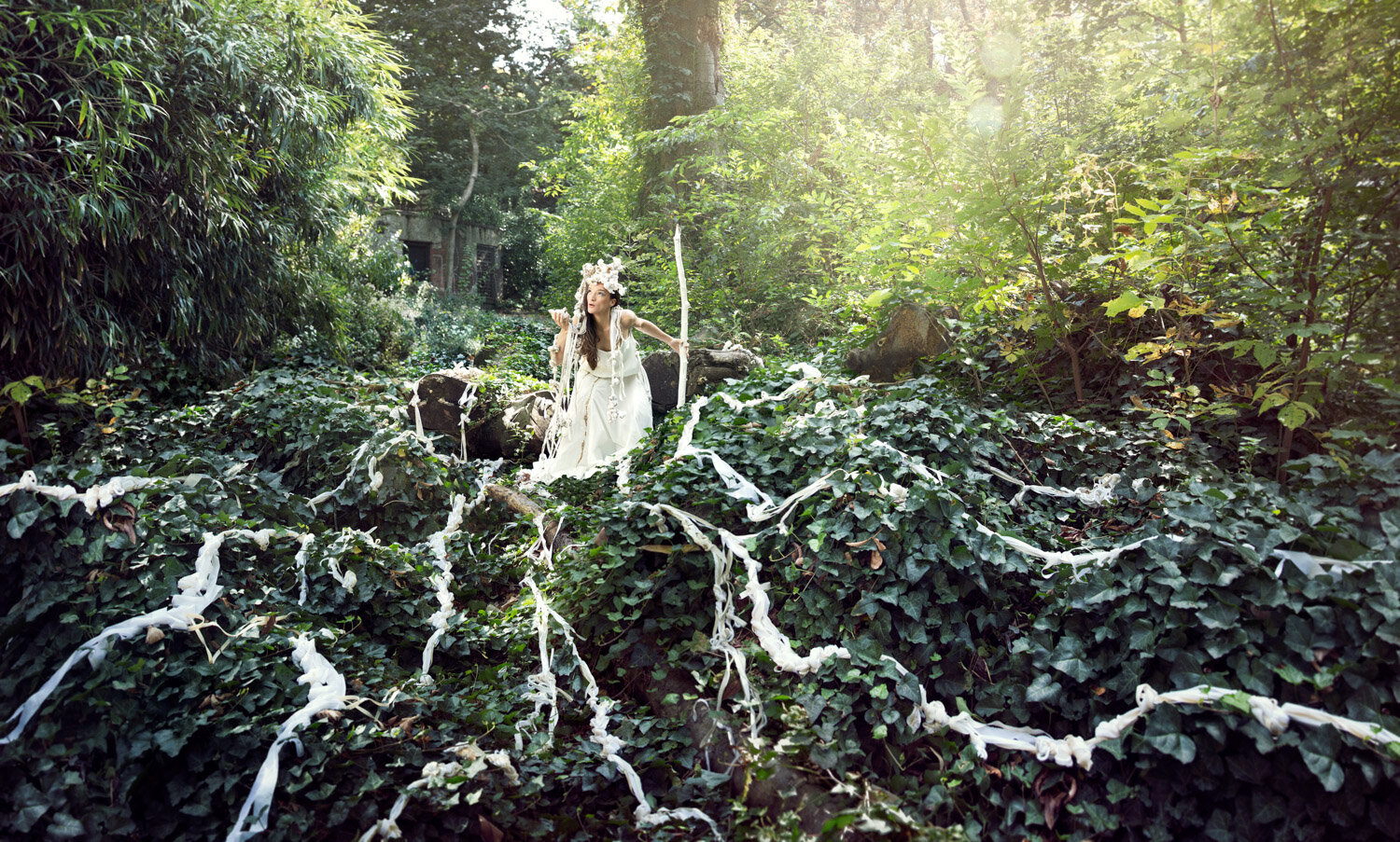 magical tendrils of knotted material flow away from woman with staff in the middle of a field of ivy