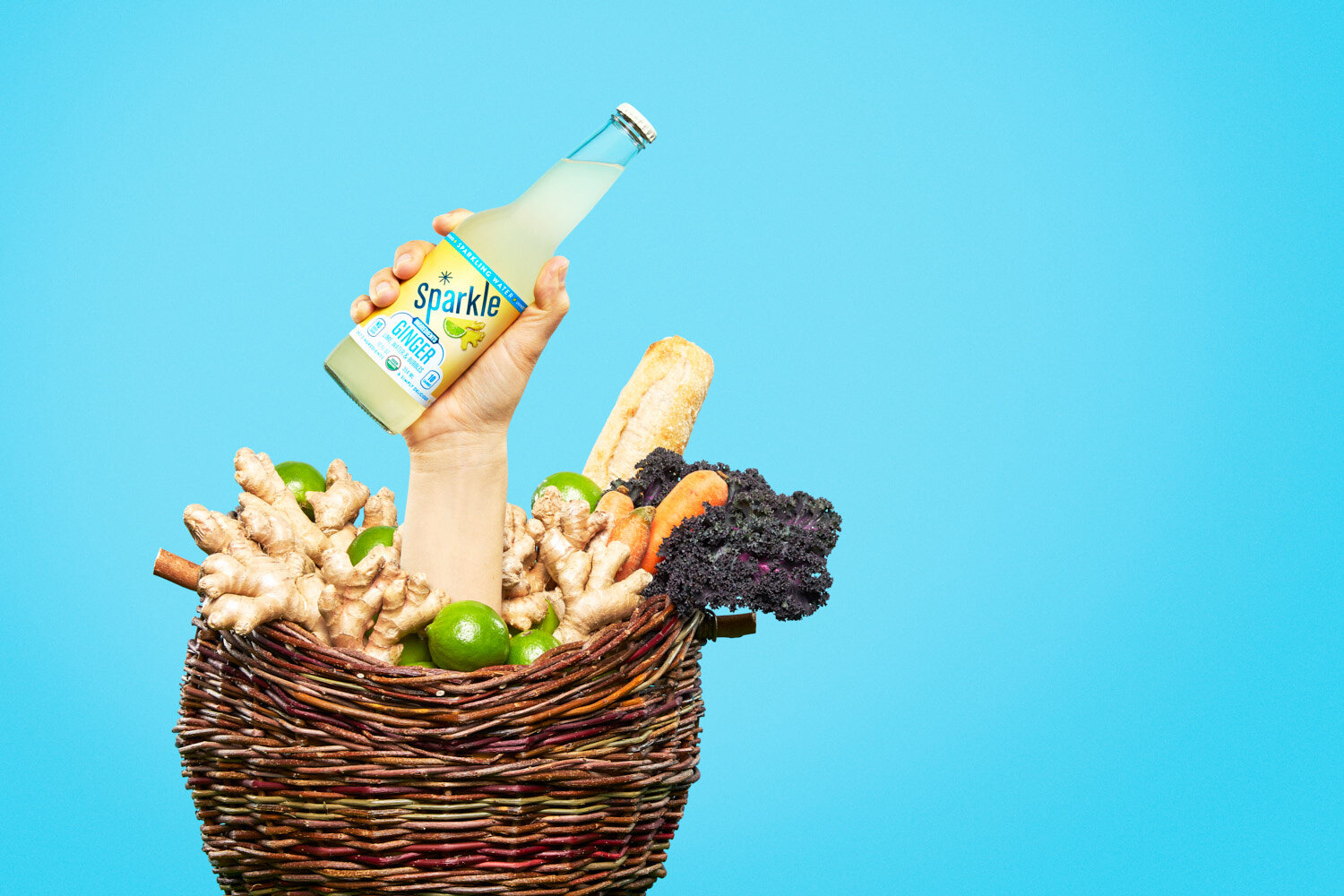Quirky product photography: hand holding a bottle of ginger Sparkle by WiscoPop! emerges from a farmers market basket full of produce.