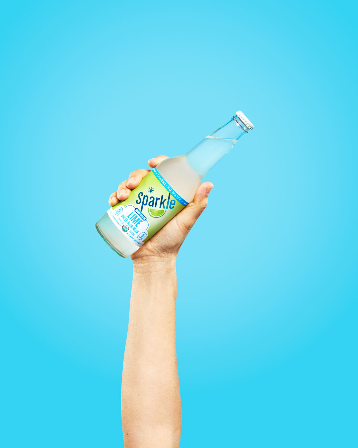Colorful beverage photography: hand holds a bottle of lime Sparkle by WiscoPop! on a blue background. 