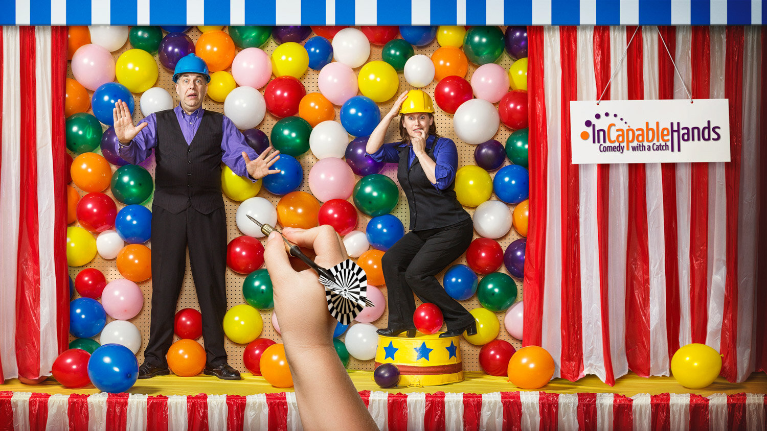 quirky promotional photo of husband and wife juggling duo Steve &amp; Kobi against a balloon wall with a kid's hand holding a dart by portrait photographer Hanna Agar