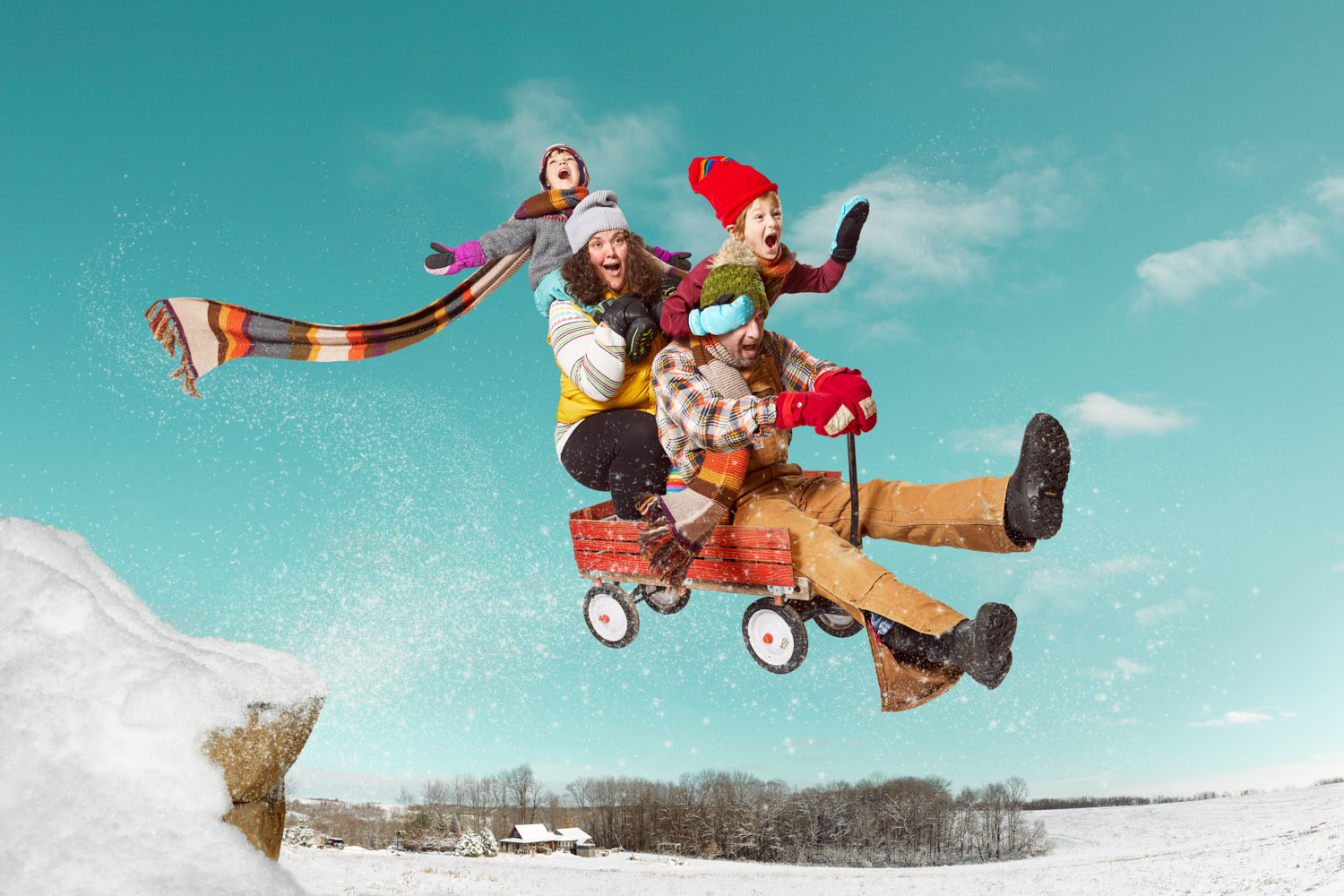 conceptual family portrait of family flying off jump in red wagon in winter by creative portrait photographer Hanna Agar in Viroqua, WI