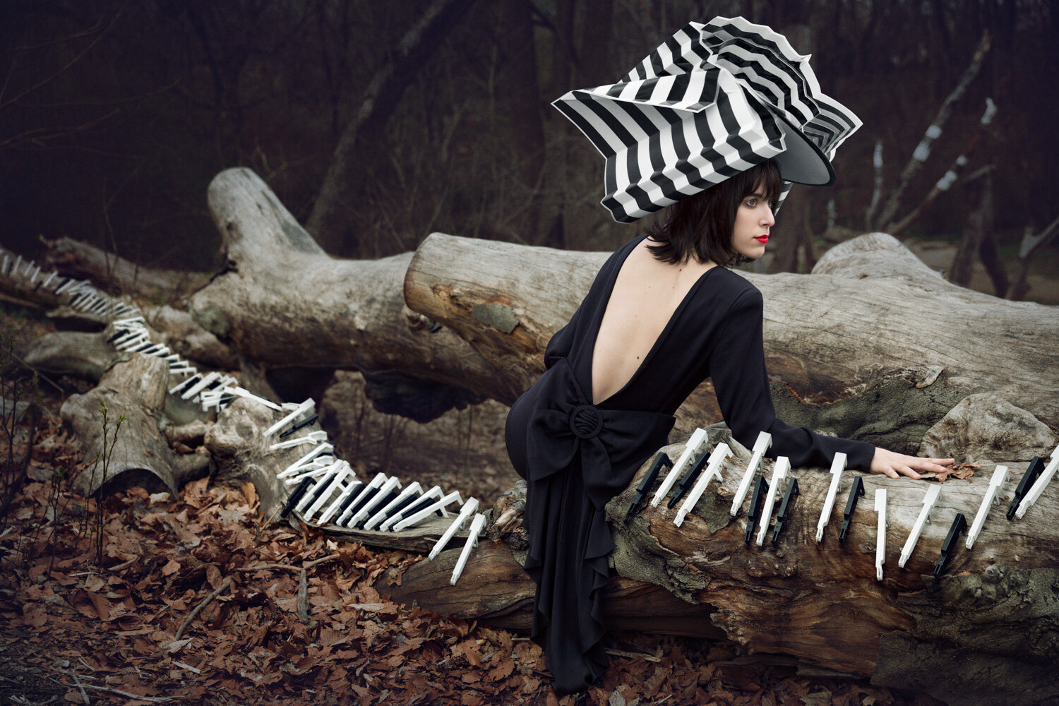 Creative portrait of musician Janna Pelle wearing a vintage open backed black dress and dramatic hat while lounging on a fallen tree that is covered in piano keys by portrait photographer Hanna Agar