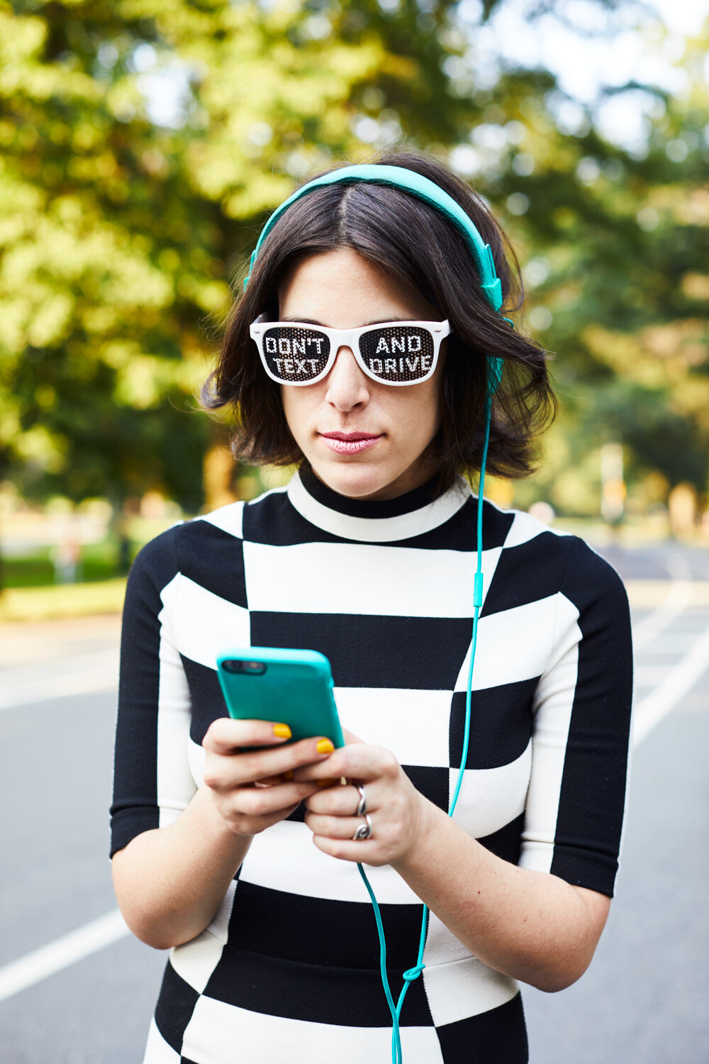 musician Janna Pelle texts on her phone while standing in the  road wearing glasses that say Don't Text and Drive for her Hit and Run album art promotional photo by portrait photographer Hanna Agar 
