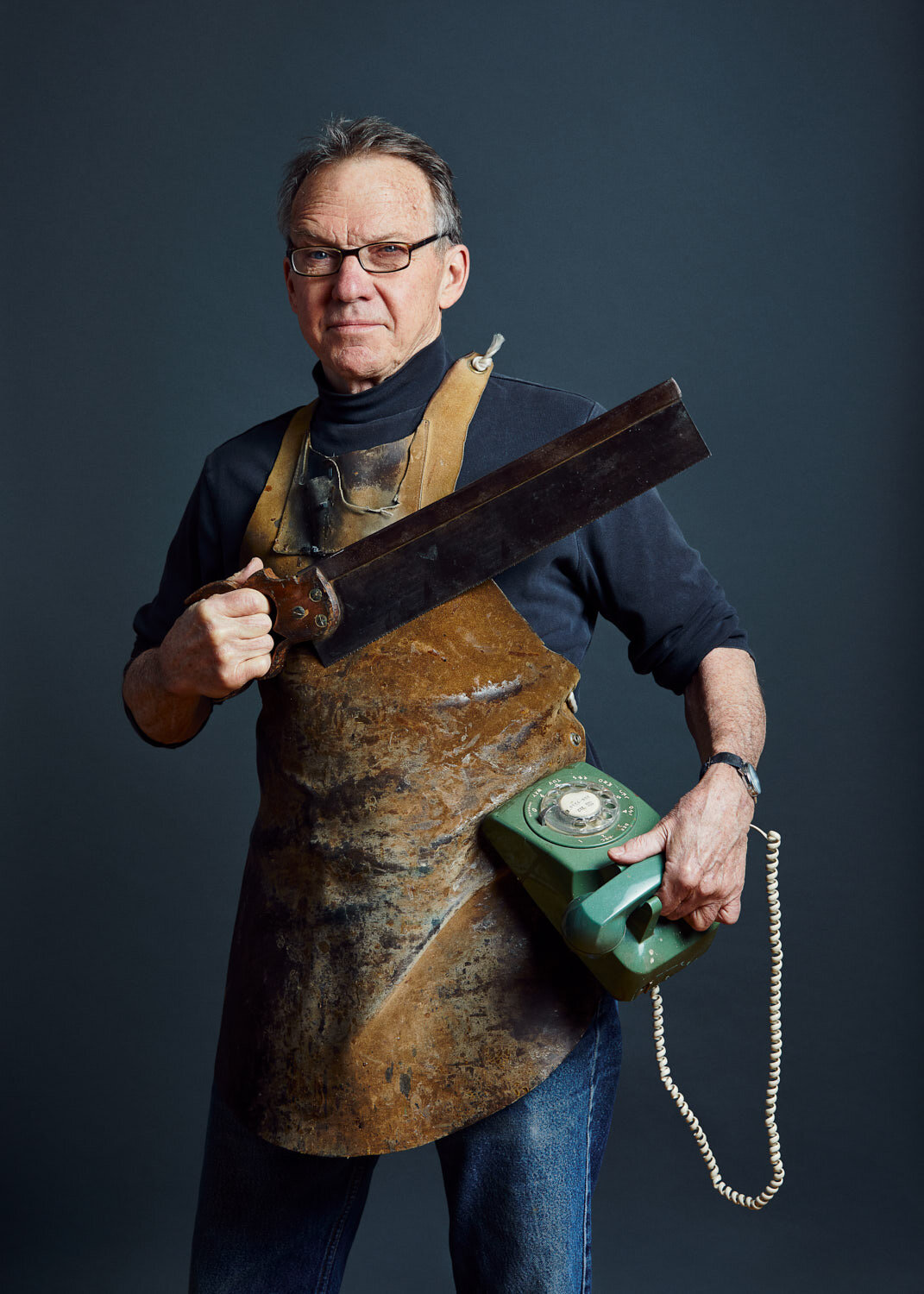 studio portrait of wood worker holding saw and green vintage phone and leather apron