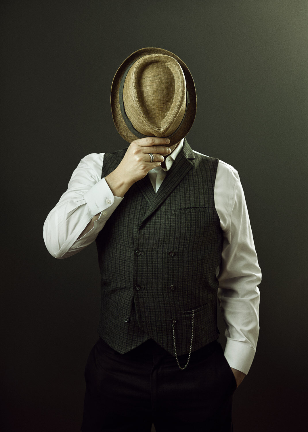 surreal studio portrait of musician in vintage outfit with hat covering his face