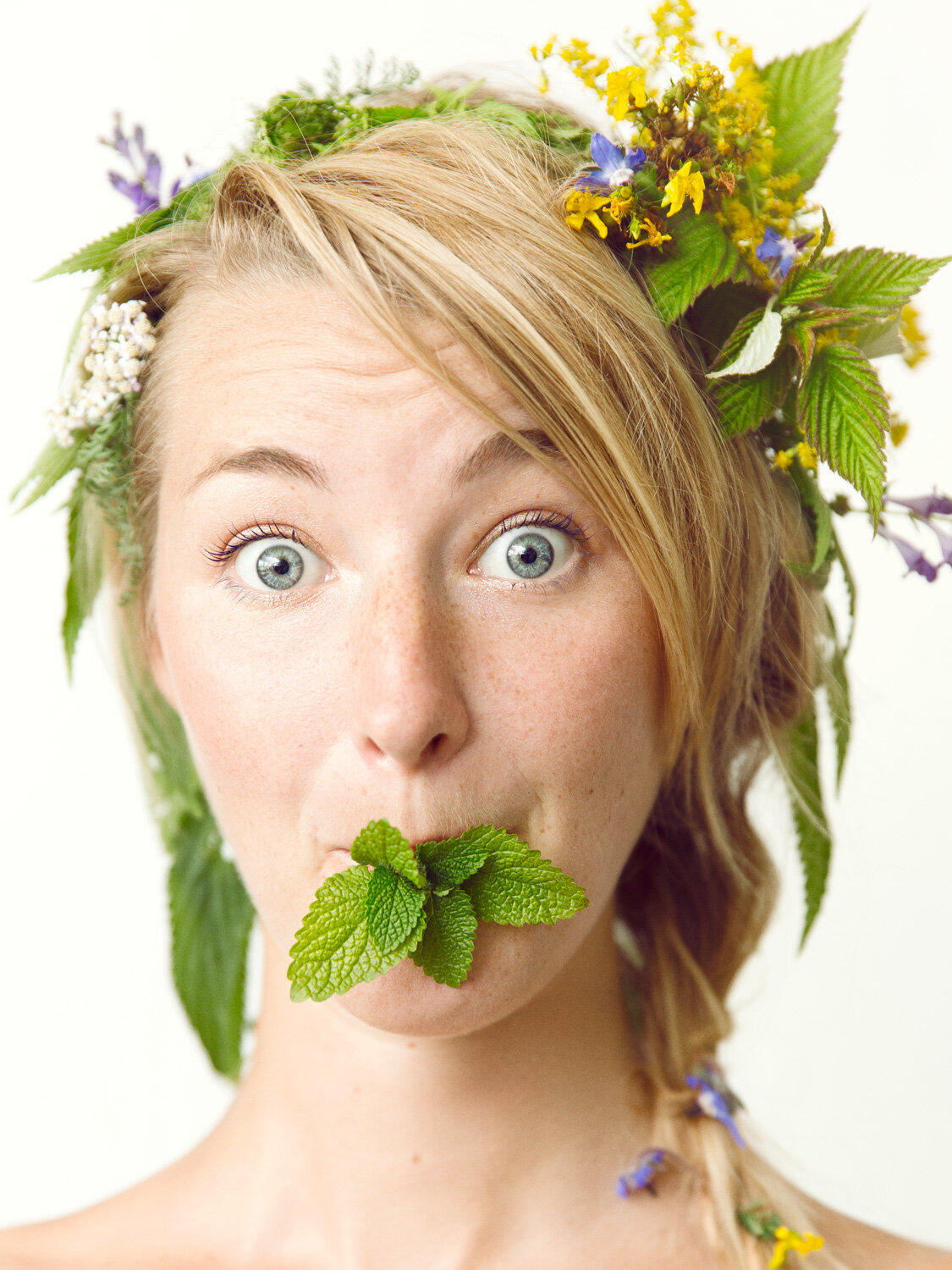 quirky portrait of herbalist woman with herbal crown making silly face with mint in mouth by portrait photographer Hanna Agar