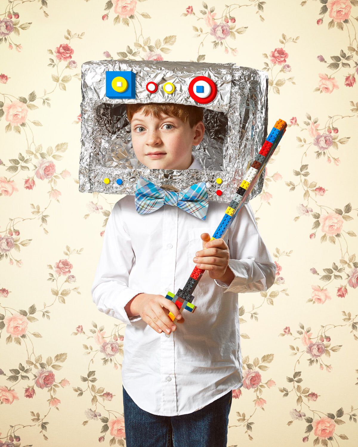 child with homemade robot head, giant bowtie, and lego sword with vintage floral wallpaper by creative portrait photographer Hanna Agar