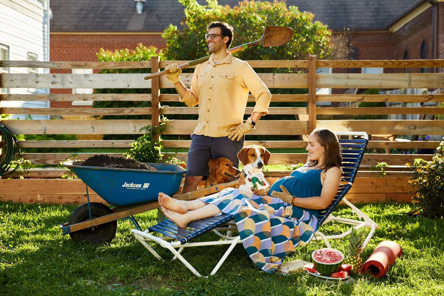 whimsical maternity portrait of mom and dad in backyard, mom reads kids book to dogs