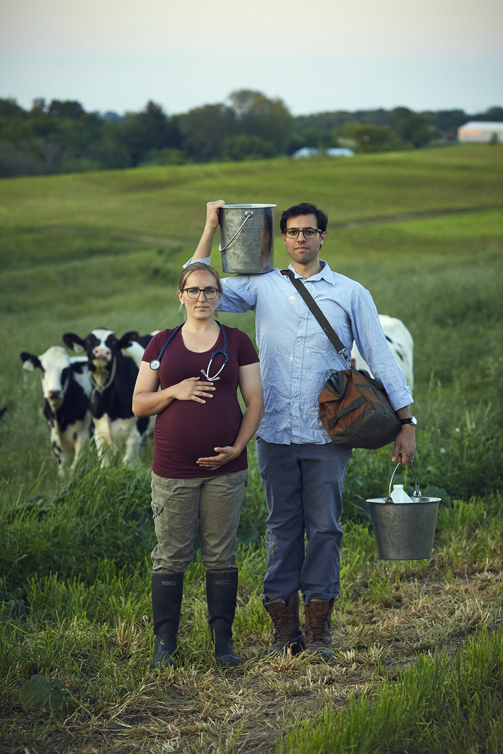 american gothic inspired maternity portrait of livestock vet in a field with cows by creative portrait photographer Hanna Agar