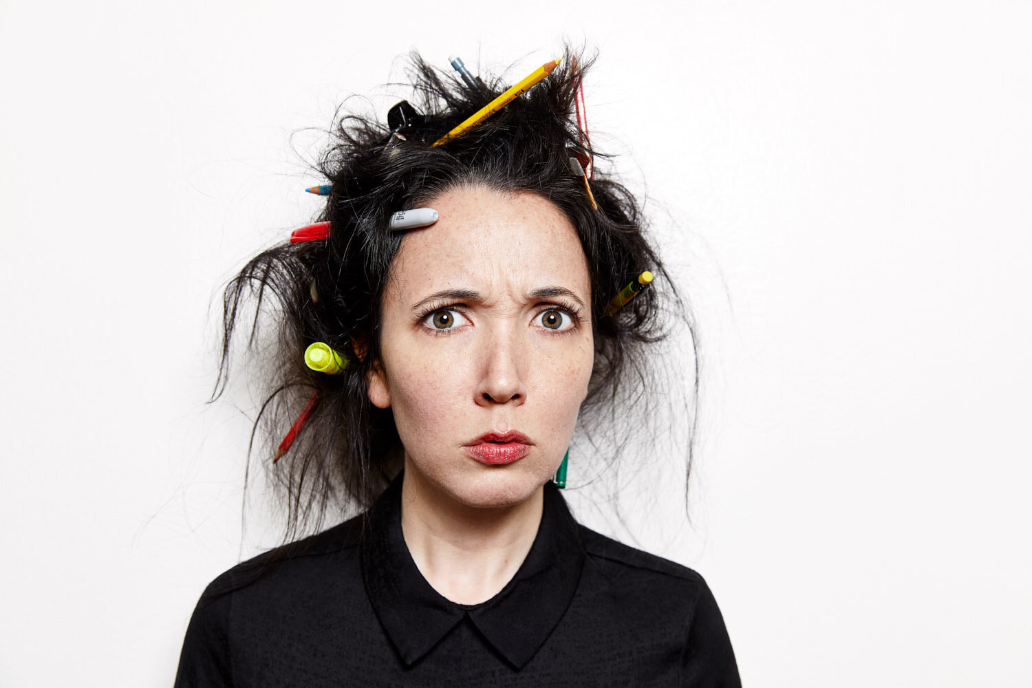quirky portrait of writer Jacqueline Raposo with pens and pencils stuck in her hair and a concerned expression 