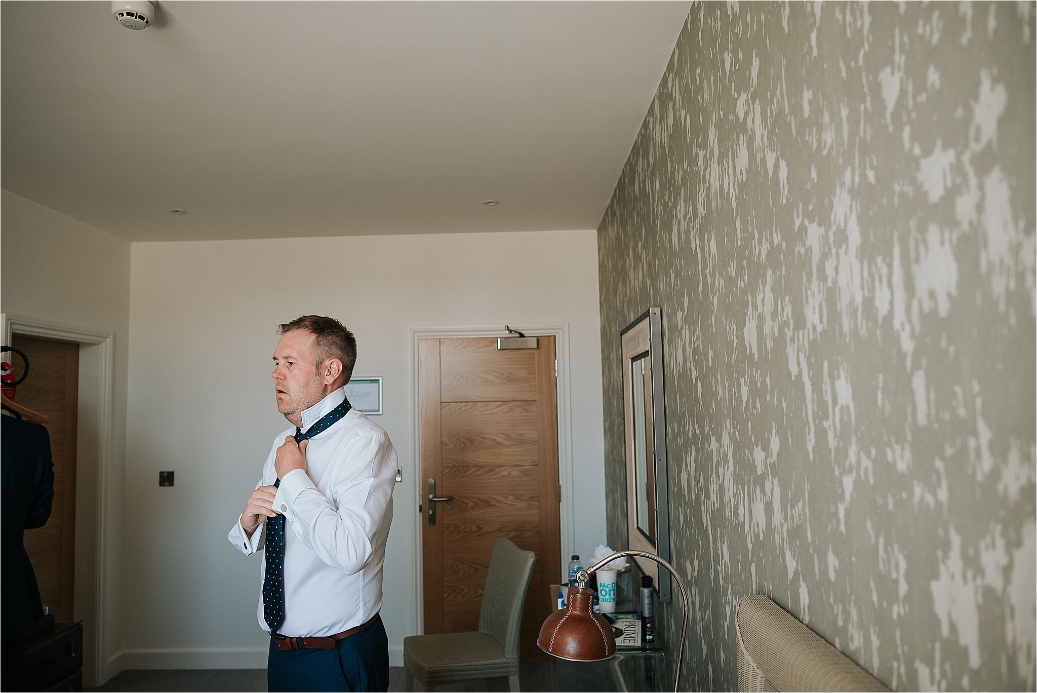 groom putting his tie on before the wedding at holmes mill 