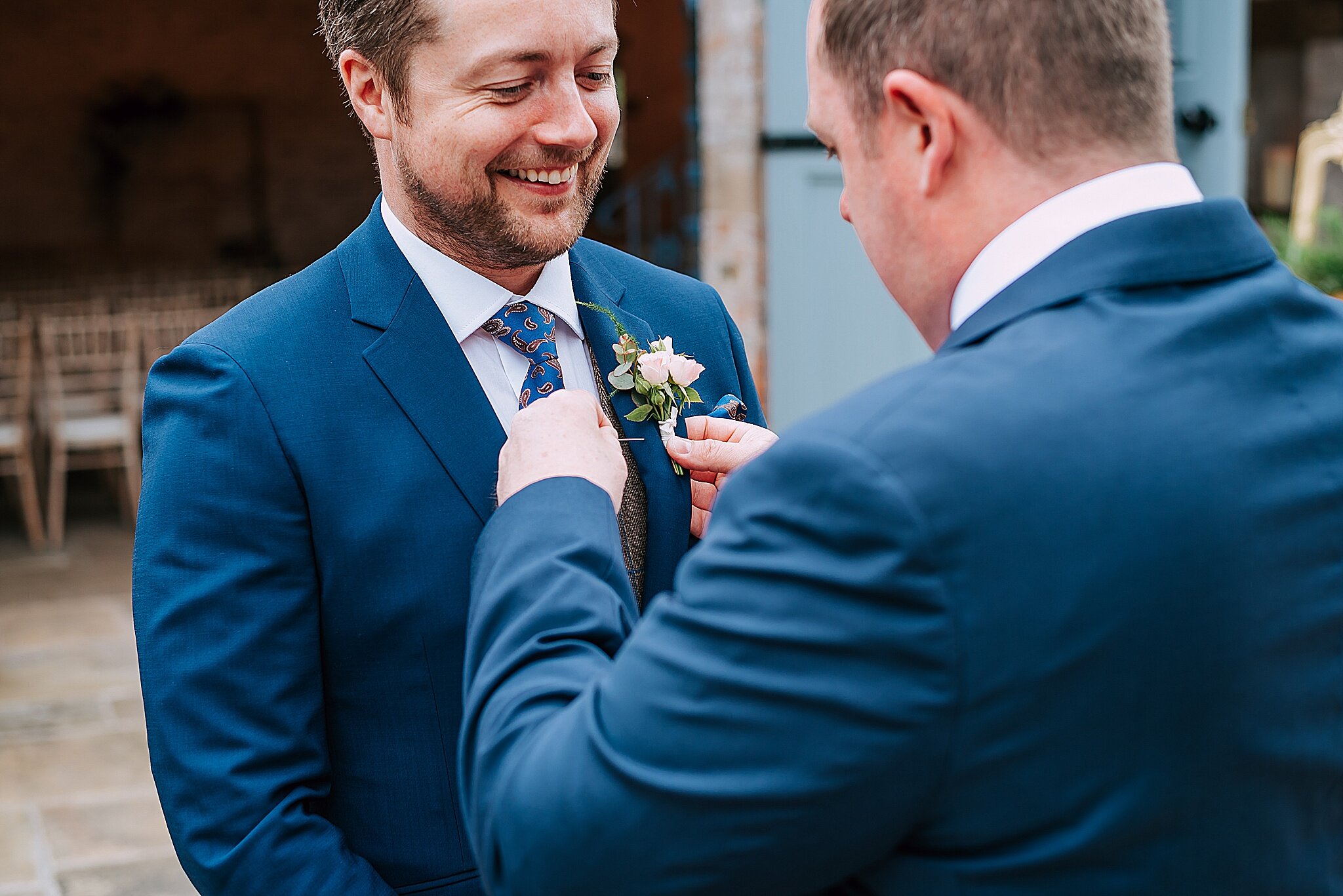 groom puts buttonhole on for wedding at dorfold hall, cheshire 