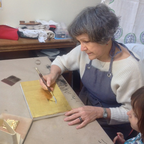 The gilder at work, burnishing the gold leaf with an agate tool. 