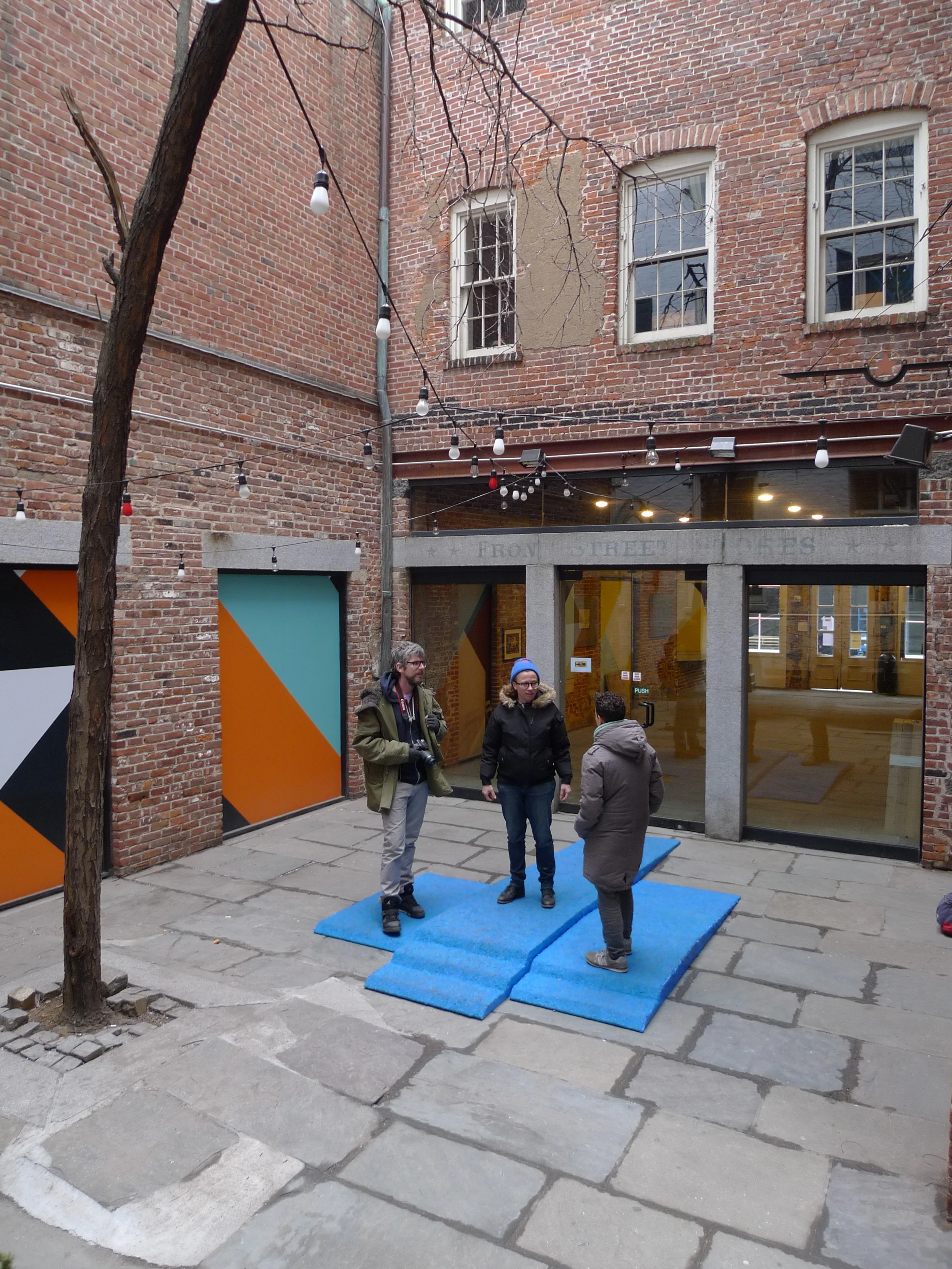   Champion Takes All , Installation view in Canon's Walk courtyard in the South Street Seaport, NYC. Visitors loitered on the podium and walked over it as they traversed the courtyard. Three piece podium, 12.5' long x 90" wide x 6" tall. Rubber granu