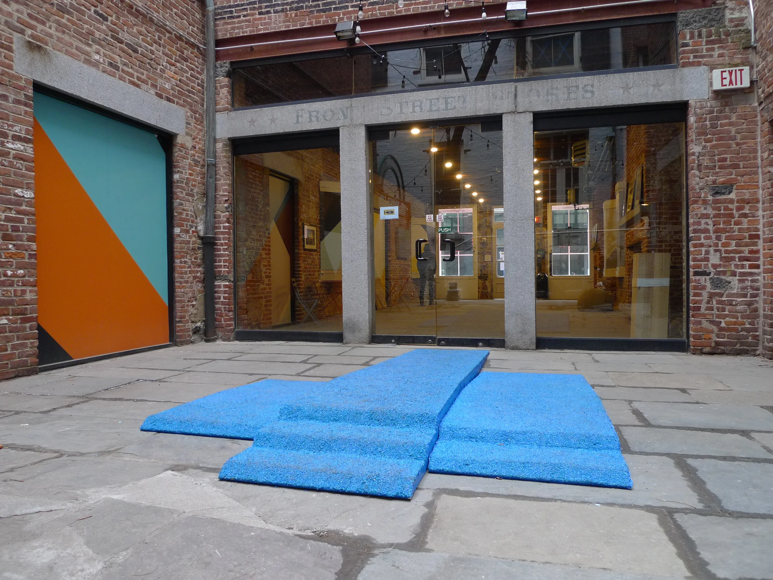   Champion Takes All , Installation view in Canon's Walk courtyard in the South Street Seaport, NYC. Visitors loitered on the podium and walked over it as they traversed the courtyard. Three piece podium, 12.5' long x 90" wide x 6" tall. Rubber granu
