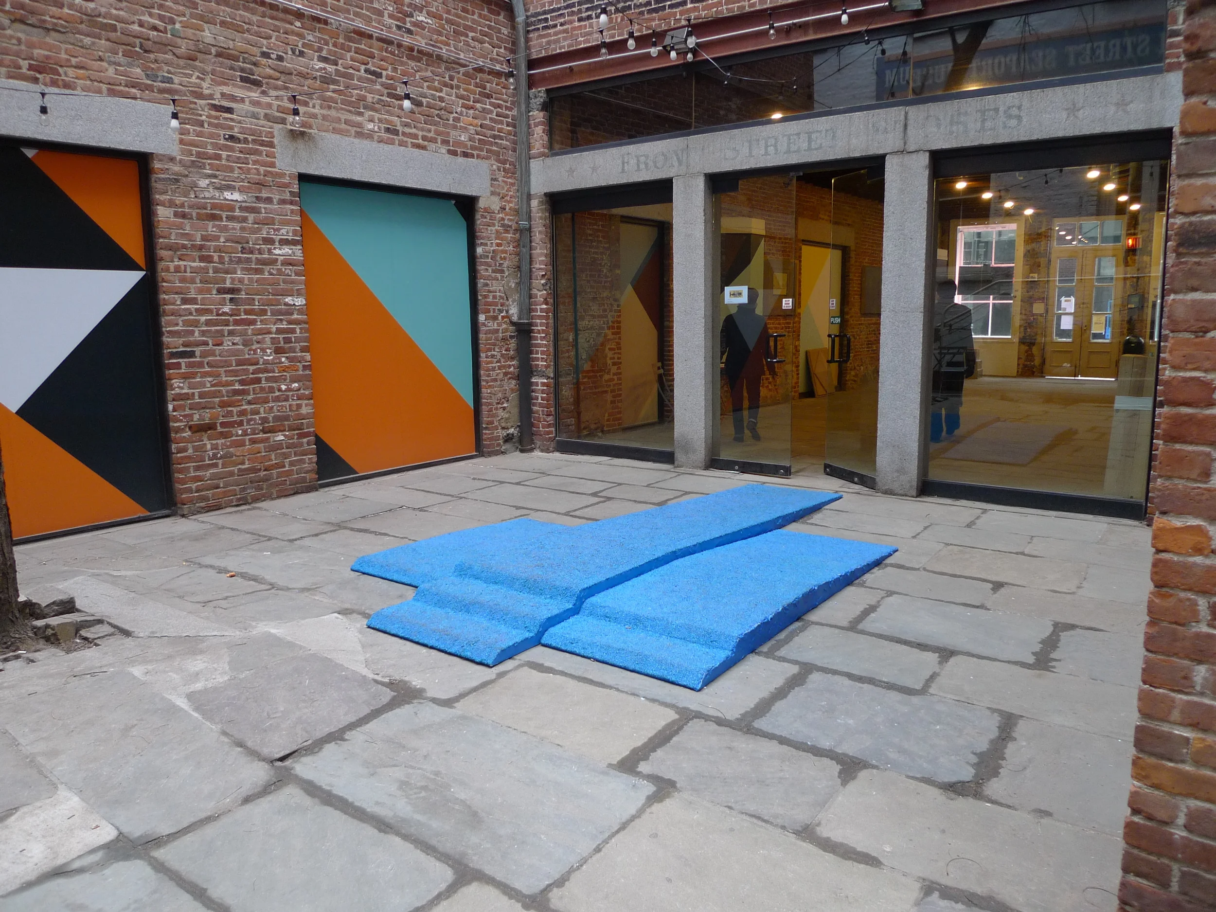   Champion Takes All , Installation view in Canon's Walk courtyard in the South Street Seaport, NYC. Visitors loitered on the podium and walked over it as they traversed the courtyard. Three piece podium, 12.5' long x 90" wide x 6" tall. Rubber granu