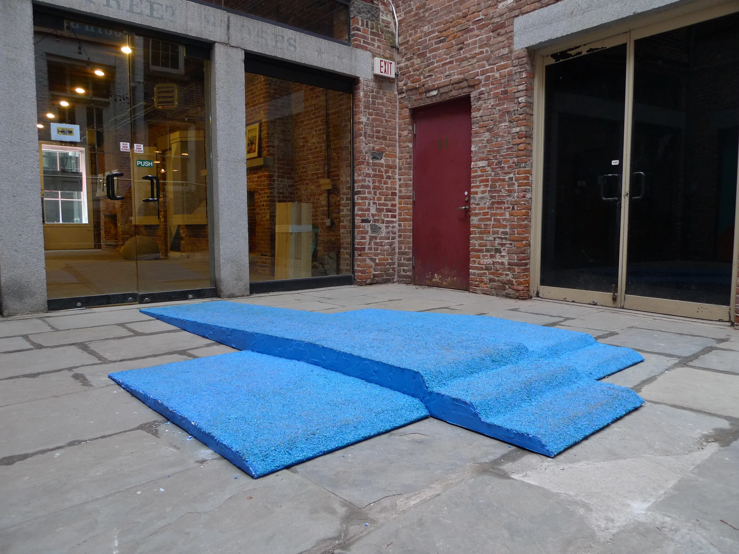   Champion Takes All , Installation view in Canon's Walk courtyard in the South Street Seaport, NYC. Visitors loitered on the podium and walked over it as they traversed the courtyard. Three piece podium, 12.5' long x 90" wide x 6" tall. Rubber granu